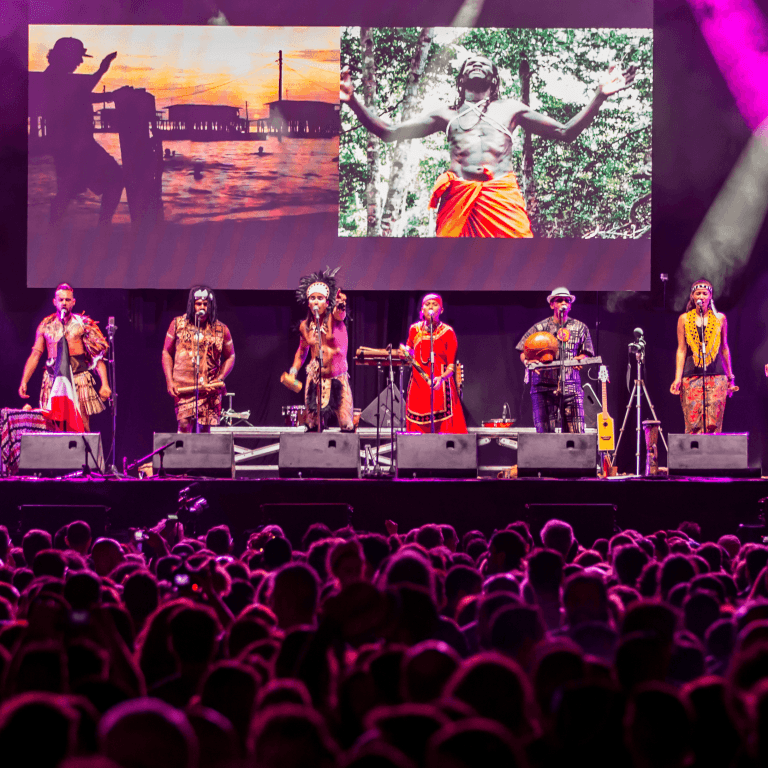 Tyynenmeren alkuperäiskansojen perinteisiin pukuihin pukeutuneita artisteja suurella festivaalilavalla.