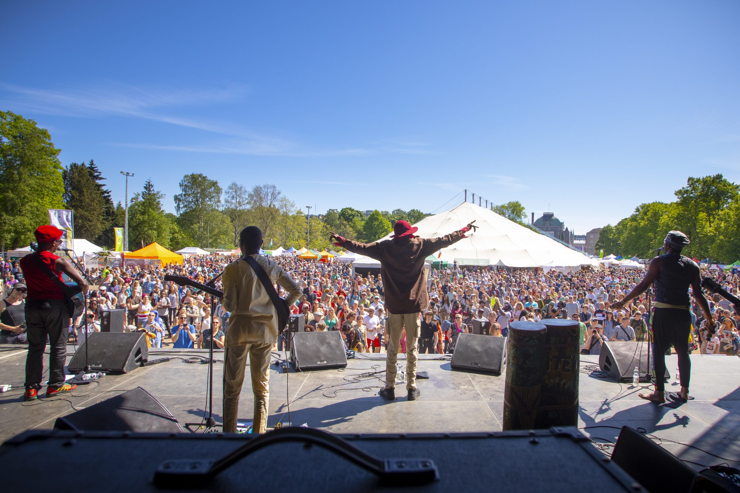 A picture taken from behind Jupiter & Okwess on stage, the artist spreading his hands and a crowd in front of the stage.